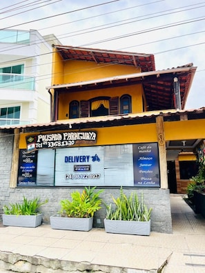 A building with a delivery service sign, a contact number, and a menu listing items like coffee, breakfast, and pizza. - Pousada Paraguaya (Angra dos Reis)