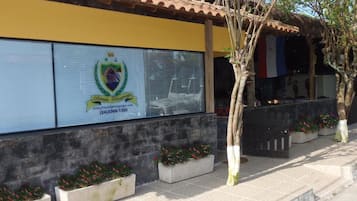 Un edificio con fachada amarilla, un logotipo con un escudo y texto, y un techo de tejas.