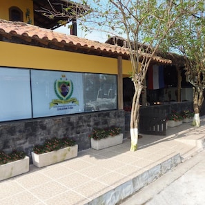 A building with a yellow facade, a logo with a crest and text, and a tiled roof. - Pousada Paraguaya (Angra dos Reis)
