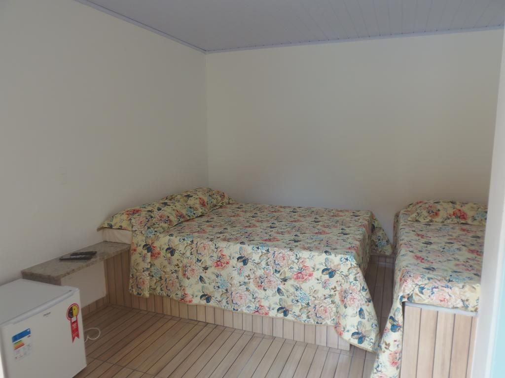 Una habitación pequeña con dos camas, piso de madera y un refrigerador blanco.