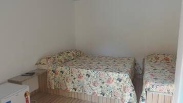 Una habitación pequeña con dos camas, piso de madera y un refrigerador blanco.