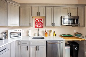 A modern kitchen with grey cabinets, a stainless steel microwave, a toaster, and a sink. - The Wheelhouse – Private 1BR near Garden of the Gods & Old Colorado City (Colorado Springs)