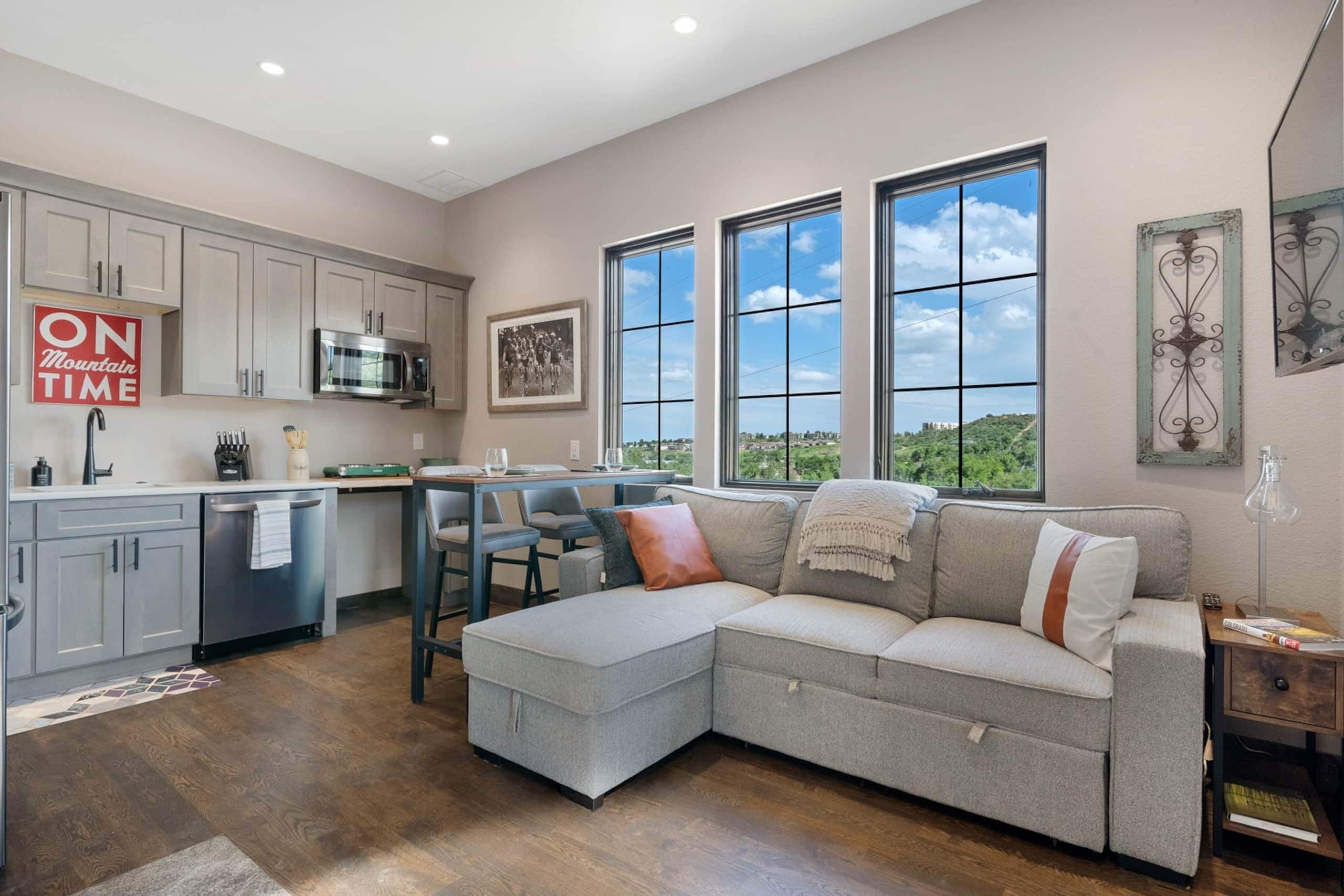 A modern kitchen with grey cabinets, a microwave, and a dining area with a grey sofa and chairs.