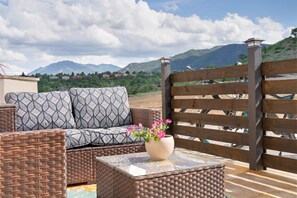 A wicker sofa with patterned cushions, a glass-top coffee table with a vase of flowers, and a wooden gate. - The Wheelhouse – Private 1BR near Garden of the Gods & Old Colorado City (Colorado Springs)