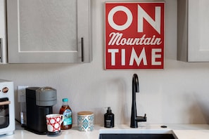 Eine Küche mit Kaffeemaschine, Tasse, Flasche, Seifenspender und Wasserhahn.
