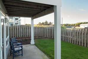 A covered patio with a wooden fence, a concrete pathway, and a seating area with two chairs. - Pickleball, Hot tub, beach access, (OBreeze) (Westport)