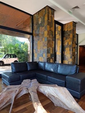 A modern interior with a black leather sectional sofa, a large wooden sculpture, and a stone wall. - Tre Iguazu Hotel (Puerto Iguazú)