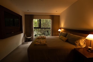 A hotel room with a large bed, a chair, a window with curtains, and a nightstand with a lamp. - Tre Iguazu Hotel (Puerto Iguazú)
