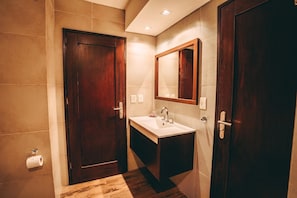 A bathroom with two wooden doors, a sink, a mirror, and a toilet paper holder. - Tre Iguazu Hotel (Puerto Iguazú)