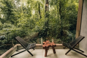 A room with a view of a dense forest through a large window, two modern chairs, and a unique wooden table. - Tre Iguazu Hotel (Puerto Iguazú)