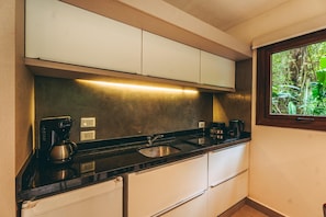 A compact kitchen with a black countertop, stainless steel sink, and white cabinets. There are two coffee makers on the counter. - Tre Iguazu Hotel (Puerto Iguazú)