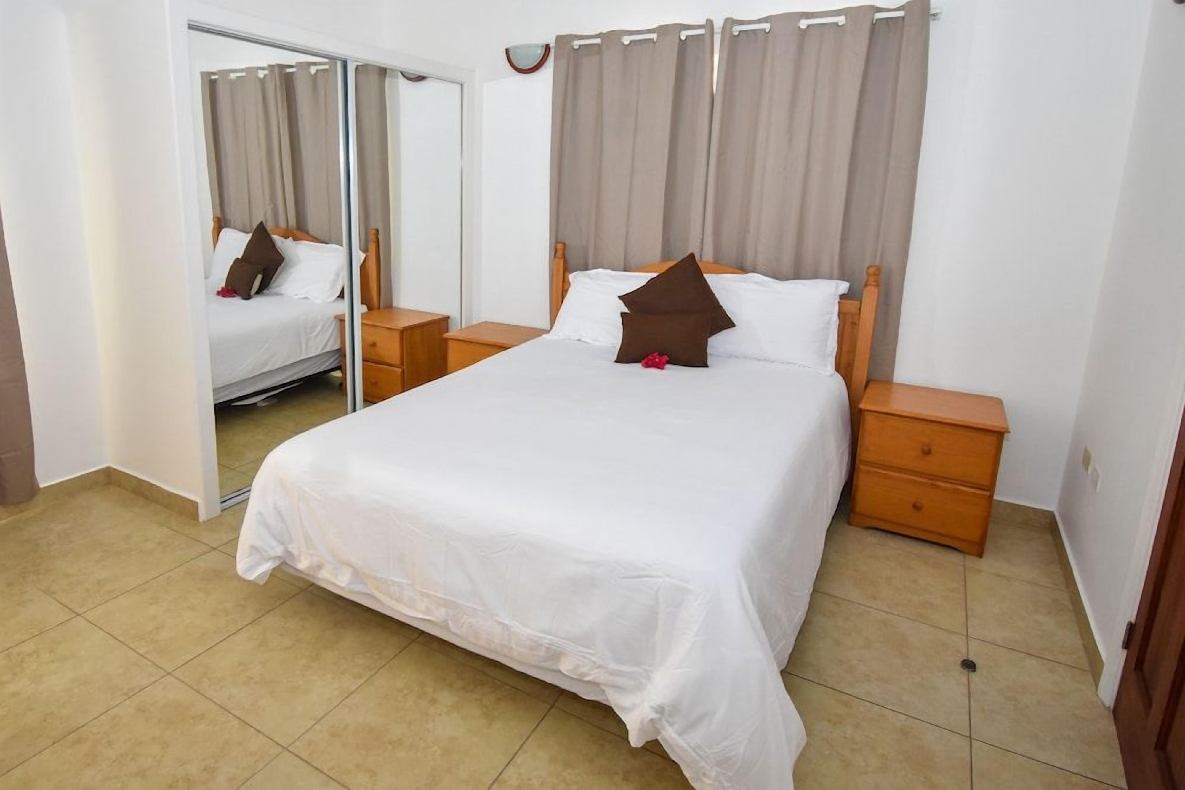 A hotel room with a bed, wooden nightstands, a mirror, and a sliding door.