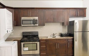 Una cocina con armarios de madera oscura, un refrigerador de acero inoxidable, un microondas, un horno y un lavamanos.