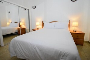 Una habitación de hotel con una cama individual, dos mesitas de noche con lámparas, un espejo y una puerta corredera.