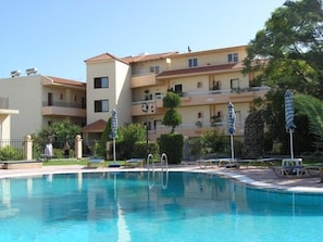 Una piscina amb gandules i ombrel·les, envoltada per un edifici d'àmbit urbà amb balcons.