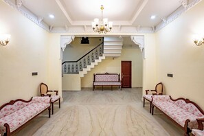 A spacious room with a marble floor, two sofas, a bench, a staircase, and a chandelier. - Justa Alwarbagh Sariska (Alwar)