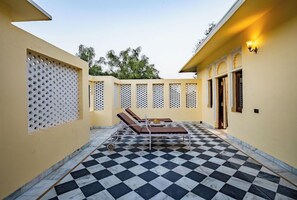A sunlit courtyard with a checkered floor, a lounge area with a table and chairs, and a wall with decorative perforated panels. - Justa Alwarbagh Sariska (Alwar)
