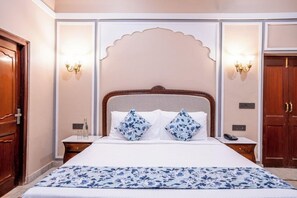 A hotel room with a large bed, two bedside tables, a nightstand, and a wooden wardrobe. - Justa Alwarbagh Sariska (Alwar)