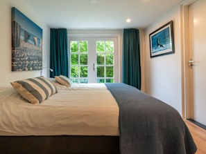 Ein Schlafzimmer mit einem Bett, einem Fenster mit Vorhängen und zwei gerahmten Bildern an der Wand.