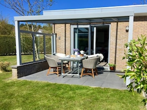 Eine moderne Außenpatio mit einer verglasten Essbereich, einer Backsteinmauer und einem gepflegten Rasen.