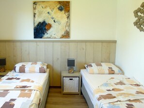 Ein Zimmer mit zwei Betten, einem Holzkopfteil, einem Wandbild und einem Nachttisch mit Lampe.