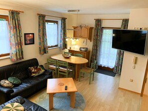 A compact living space with a sofa, dining table, chairs, a television, and a kitchenette area. - Family Relax Carinthia Love (Feistritz im Rosental)