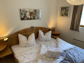 A hotel room with a bed, two nightstands, a wall-mounted picture, a window with curtains, and a ceiling light fixture. - Family Relax Carinthia Love (Feistritz im Rosental)