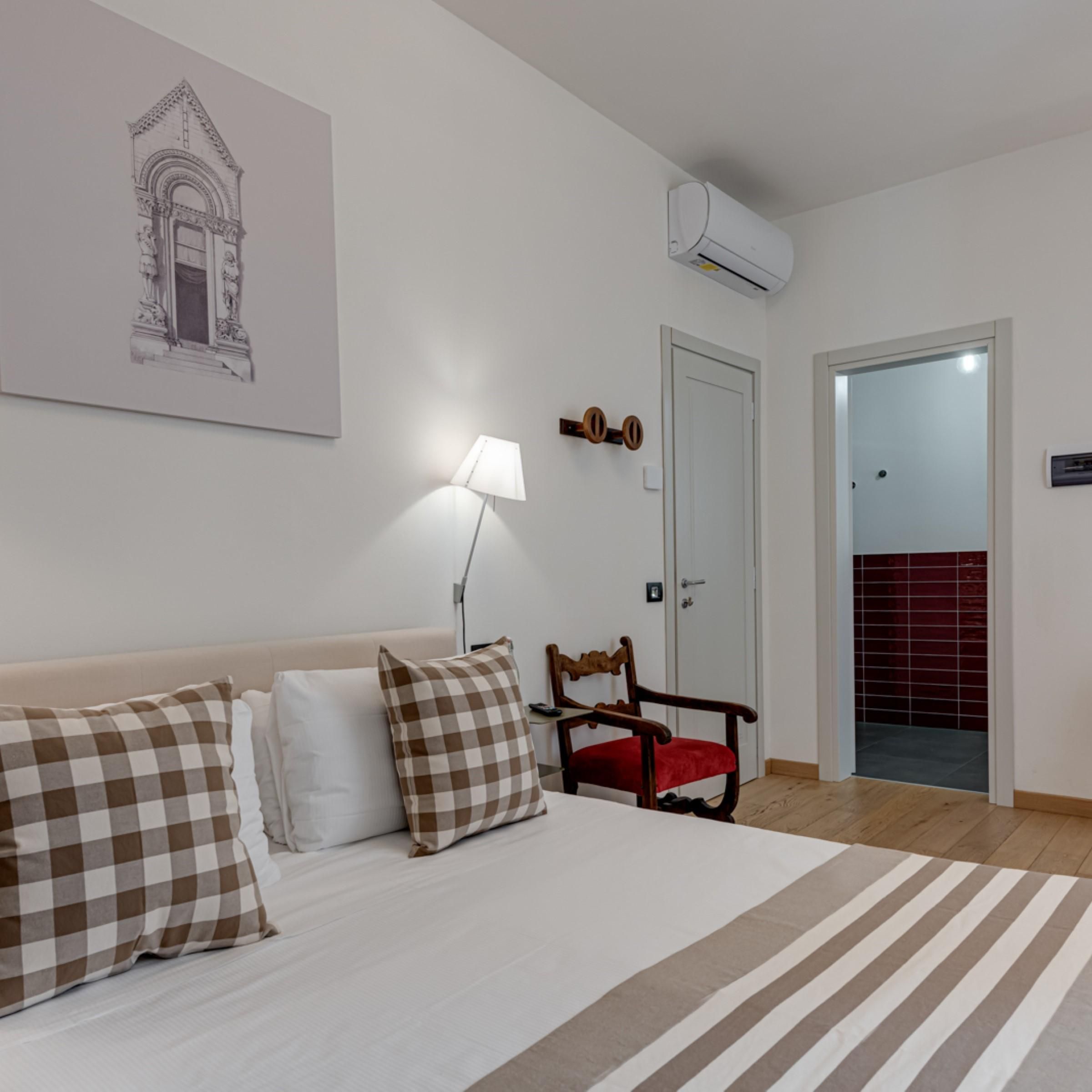 Ein Schlafzimmer mit einem Bett, einem Sessel, einer Lampe, einer Tür und einer Klimaanlage.