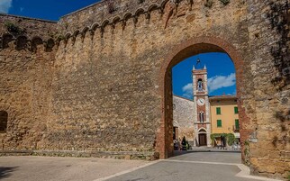 Un arco de piedra que da acceso a un edificio con una torre de campanas y un reloj.