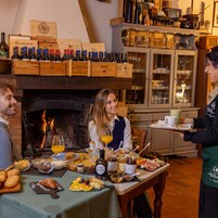 A cozy dining area with a fireplace, a variety of food and drinks on the table, and wine bottles displayed on shelves above.