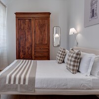 Un dormitorio con un armario de madera grande, una mesita de noche con lámpara y una cama con ropa de cama a rayas.