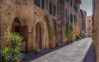 A cobblestone street lined with historic stone buildings, featuring arched doorways and potted plants.
