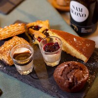 Una bandeja de postres con pastelería, una porción de pastel y dos vasos pequeños de una bebida cremosa.