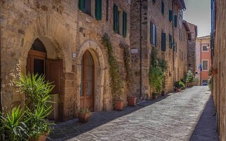 Calle adoquinada flanqueada por edificios históricos de piedra, con arcos y macetas con plantas.