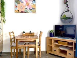 Ein Zimmer mit einem Holztisch und -stühlen, einem Fernseher auf einem Holzschrank und einer an der Wand befestigten Pflanze.