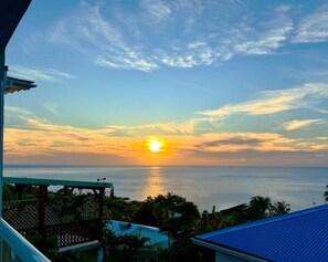 Ein Sonnenuntergangsblick von einem Balkon mit Blick auf ein Gewässer, bewölkter Himmel und ferne Horizontlinie.