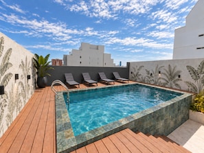 Una piscina en la azotea con cubierta de madera y sillas de descanso.