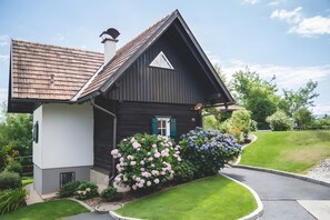Ein kleines, dunkles Holzhaus mit geneigtem Dach, einer weißen Tür und der Hausnummer 15 an der Wand.