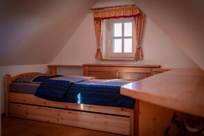 Ein Schlafzimmer mit einem hölzernen Bett, einem Fenster mit Vorhängen und einer schrägen Decke.