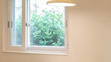 A room with a white table and two chairs, a window with a view of greenery, and a hanging light fixture.