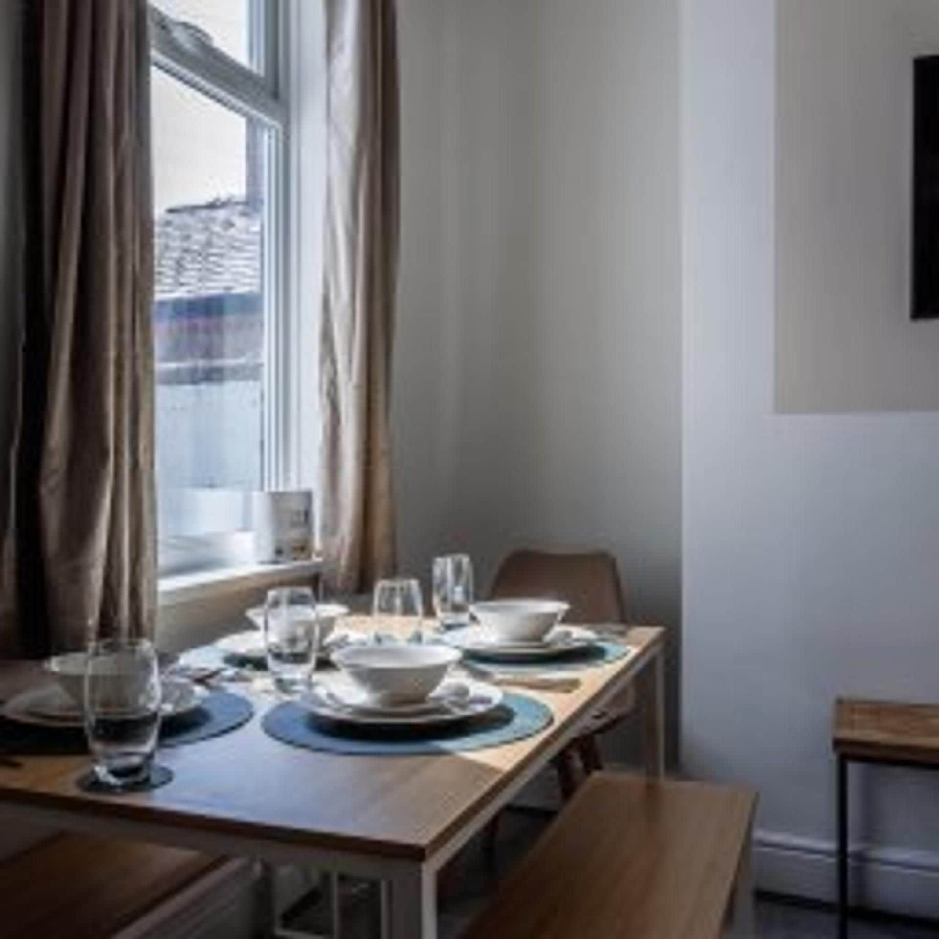 A dining area with a table set for two, a window with curtains, and a wall-mounted television.