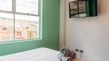 Une chambre d’hôtel avec un lit, une fenêtre donnant sur la ville et un téléviseur fixé au mur.