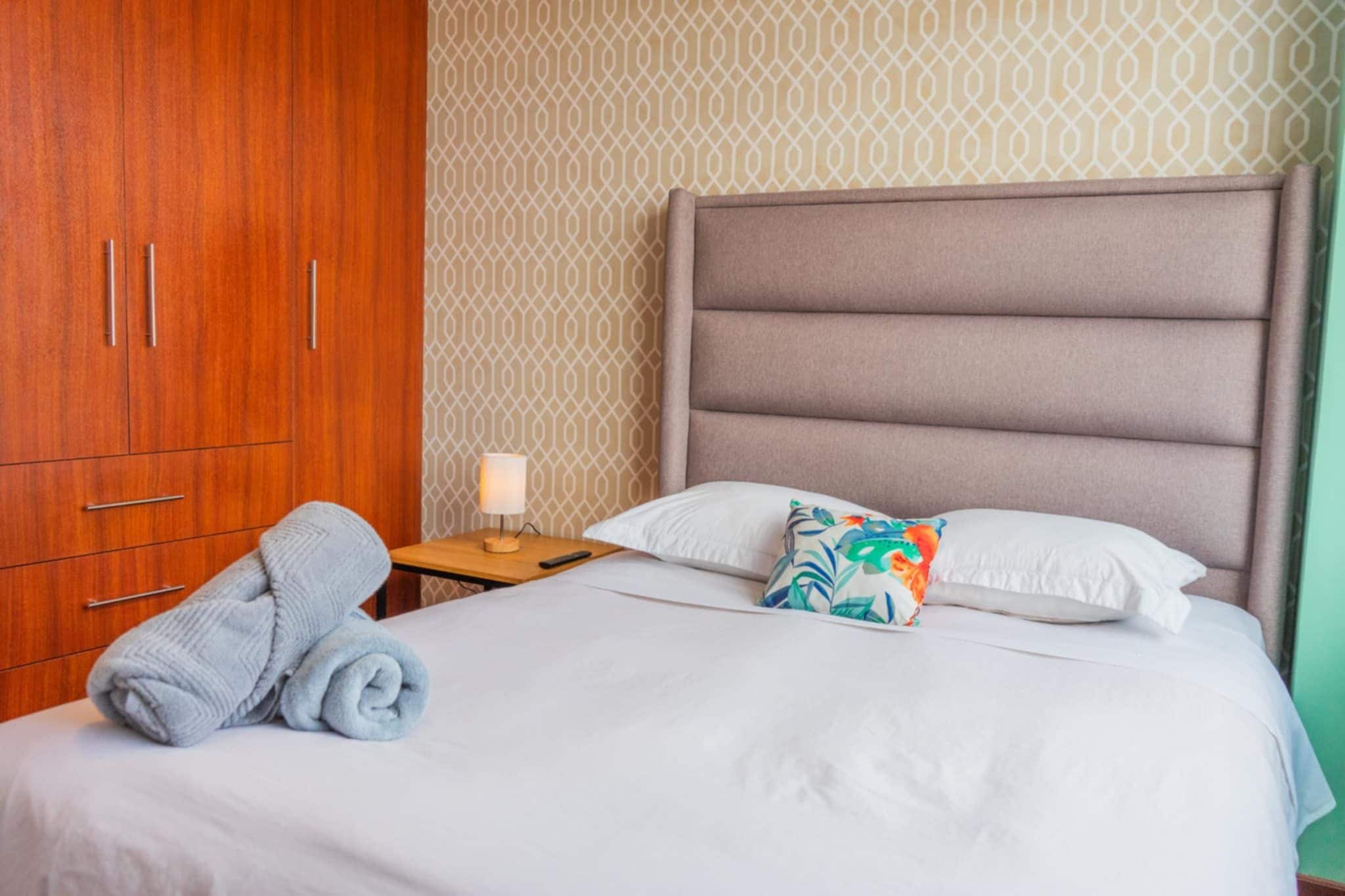 Ein Hotelzimmer mit einem Bett, einem Holzschrank, einem Nachttisch mit Lampe und einem blumigen Kissen.