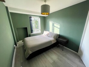Et soveværelse med en seng, et natbord, et vindue og en radiator.