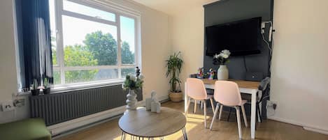 Una sala de estar moderna con comedor, ventanas amplias, televisor de pantalla plana y una planta en maceta.