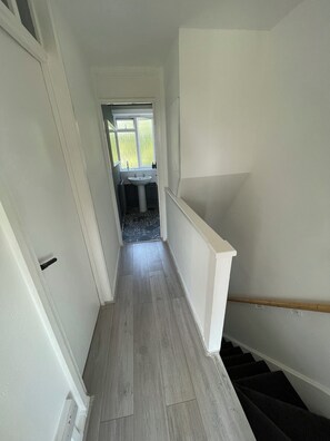 Ein schmaler Flur mit Holzboden, einer weißen Tür links und einem Fenster am Ende.
