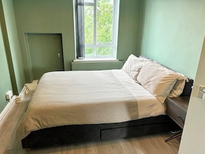 Ein Schlafzimmer mit Bett, Fenster, Heizkörper und Tür.
