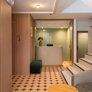 A hotel lobby with a reception desk, a green bench, and a patterned floor. - Hotel Papa Ratchada-huai Khwang (Bangkok)