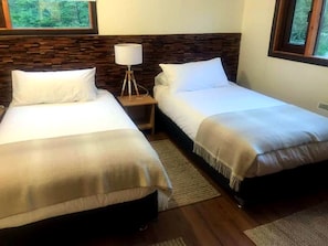 Habitación de hotel con dos camas individuales, una mesita de noche con lámpara y vista al exterior por una ventana.