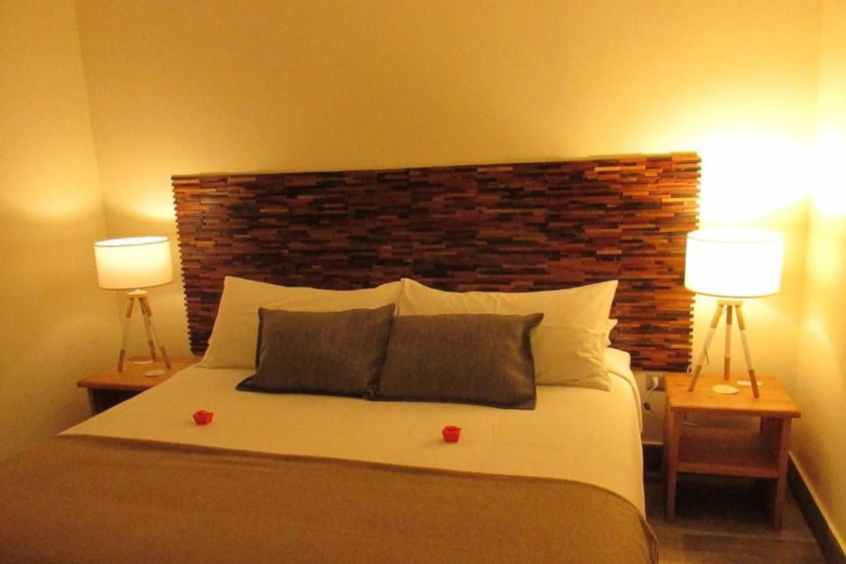 A hotel room with a bed, two bedside lamps, and a wooden headboard.